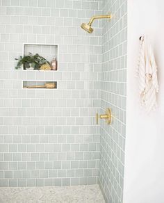 a white tiled shower with gold fixtures and shelves