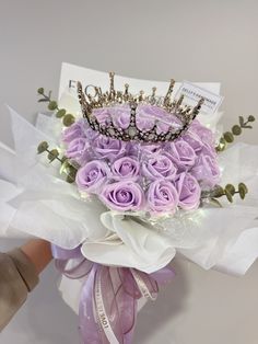 a bouquet of purple roses with a tiara on top is being held by someone's hand