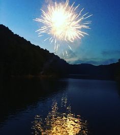 fireworks are lit up in the sky over water and hills at night with reflections on the surface