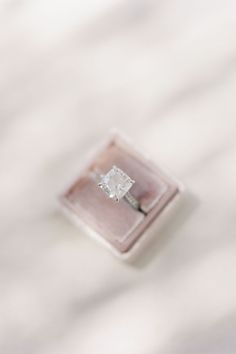 an engagement ring sitting on top of a white cloth covered tablecloth with a diamond in the center