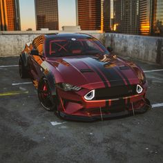 a red sports car with black stripes parked in a parking lot next to tall buildings