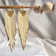 two pairs of earrings hanging from a wooden stick on a white cloth covered sheet background