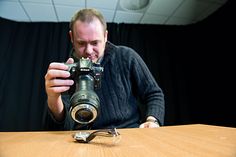 a man taking a photo with his camera on a wooden table in front of a black curtain