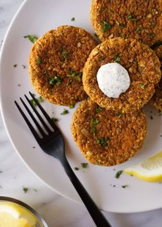 three crab cakes on a white plate with lemon wedges and a fork next to it