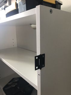 a white shelf with two black latches on it's sides and a yellow object in the background