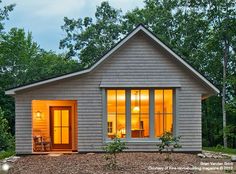 a small house is lit up at night in the woods with trees and shrubs surrounding it