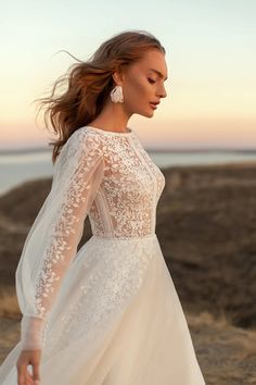 a woman in a wedding dress is standing on the beach at sunset with her hair blowing in the wind