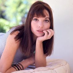 a woman laying on top of a bed with her hand under her chin and looking at the camera