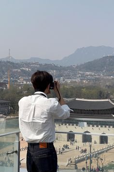 a man standing on top of a building looking at the city below him with his cell phone to his ear