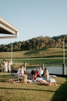 several people are sitting on the grass near a lake and picnicking at an outdoor event