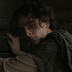 a young man with curly hair and glasses is leaning against a wall in the dark