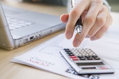 a person using a calculator on top of a desk next to a laptop