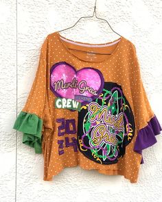 an orange shirt with purple and green designs on it hanging from a white brick wall