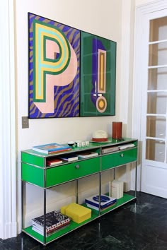 a green console unit in front of a painting and bookshelf on the wall