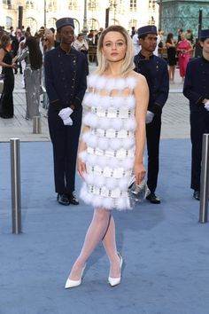 a woman in a white dress standing on a blue carpet with other people behind her