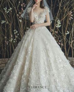 a woman wearing a wedding dress with a veil on her head and flowers in the background