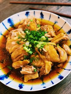 a white and blue bowl filled with food on top of a wooden table next to chopsticks