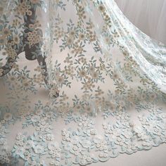 a white and blue lace with flowers is on the ground next to a curtain that has sheer fabric over it