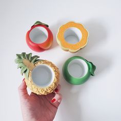 a hand is holding three cups with fruit in them and one has a pineapple on it