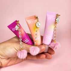 three lip balm tubes in the palm of someone's hand with pink pom - poms