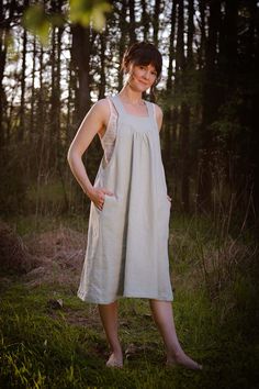 a woman is standing in the woods wearing a white dress and smiling at the camera