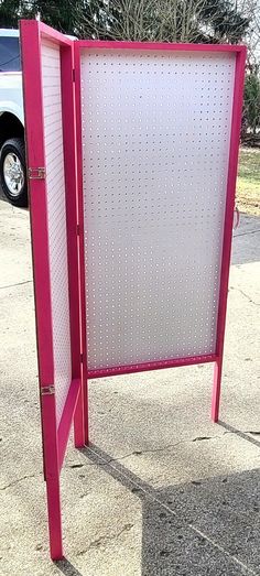 a pink sign sitting on the side of a road next to a parking lot with a white car in the background