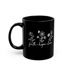 a black coffee mug with white flowers and the words faith hope love written on it