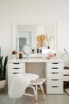 a white desk with drawers and a mirror on top of it next to a potted plant