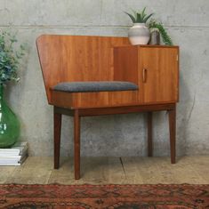 a wooden cabinet sitting next to a green vase on top of a carpeted floor