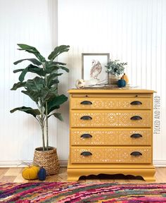 a yellow dresser sitting next to a potted plant on top of a wooden floor