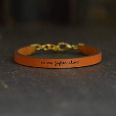 A perfect reminder of solidarity, our No One Fights Alone Inspirational Leather Bracelet is perfect for everyday encouragement. This bracelet reads "no one fights alone" in lowercase lettering. Writing has been engraved/burned into leather. Small and delicate writing adds charm to the design.Finishes + Details: Leather bracelet. Include a metal chain extender. Metal details are made from brass.Sizing Information: 9" total bracelet length.Dimensions: Leather is approximately 2mm thick. Bracelet i Engraved Leather Bracelets, Bible Verse Jewelry, Graduation Gifts For Daughter, Best Friend Bracelets, Awareness Jewelry, Bracelet Quotes, Leather Bracelets Women, Sisters By Heart, Sister Bracelet