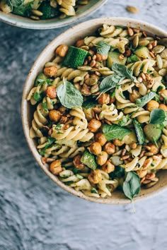 two bowls filled with pasta and vegetables on top of a marble countertop next to each other