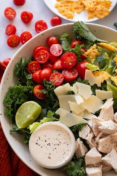 A bowl of kale caesar salad on a table. There are some grape tomatoes and parmesan crisps scattered nearby. Salad Copycat, Copycat Recipe