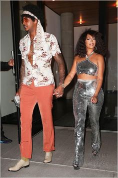 the man and woman are dressed up in disco outfits, one is holding his hand