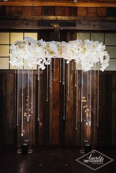 an arrangement of white flowers hanging from the ceiling in front of a wooden paneled wall