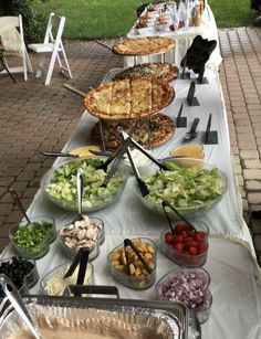 an outdoor buffet with pizzas and salads on the table in front of it