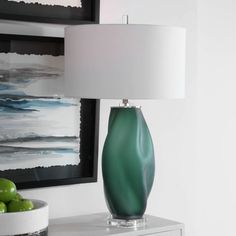 a green vase sitting on top of a table next to a lamp