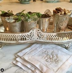 there is a tray with silver cups and plants in it on top of the table