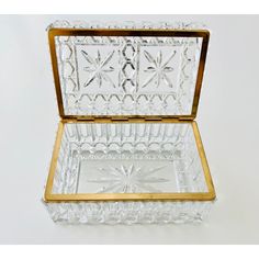 a clear glass box with gold trimmings on the lid and bottom, sitting on a white surface