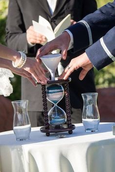 the bride and grooms hands are pouring sand into an hour - glass at their wedding ceremony