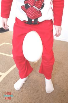 a man in red pants and white shirt holding a white frisbee while standing on carpet