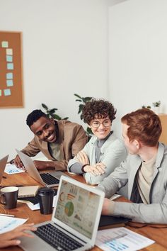 four people sitting at a table with laptops and papers in front of them, all smiling