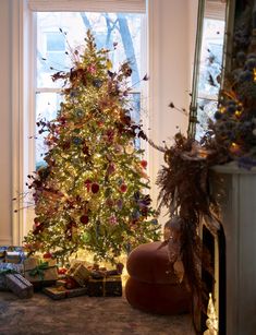 a decorated christmas tree sitting in front of a window next to a fire place with presents on the floor