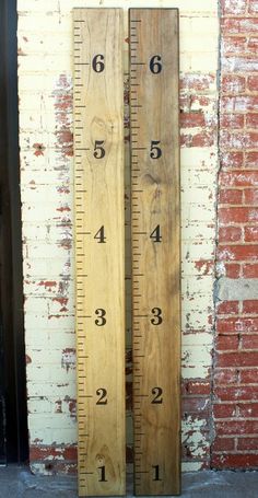 a tall wooden ruler sitting next to a brick wall