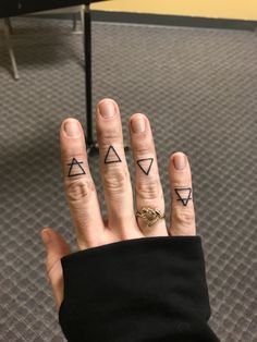 a woman's hand with three small triangle tattoos on it, and two fingers