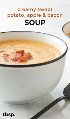 a bowl of soup with bacon in it and two spoons next to it on a white table