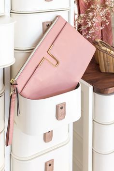 a pink purse sitting on top of a white dresser next to drawers and a basket