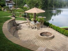 an outdoor patio with table and chairs next to a body of water in the background