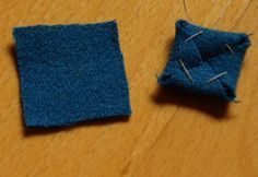 two pieces of blue fabric sitting on top of a wooden table next to a sewing needle