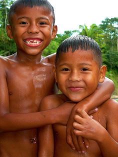 two young boys standing next to each other in the water with their arms around one another